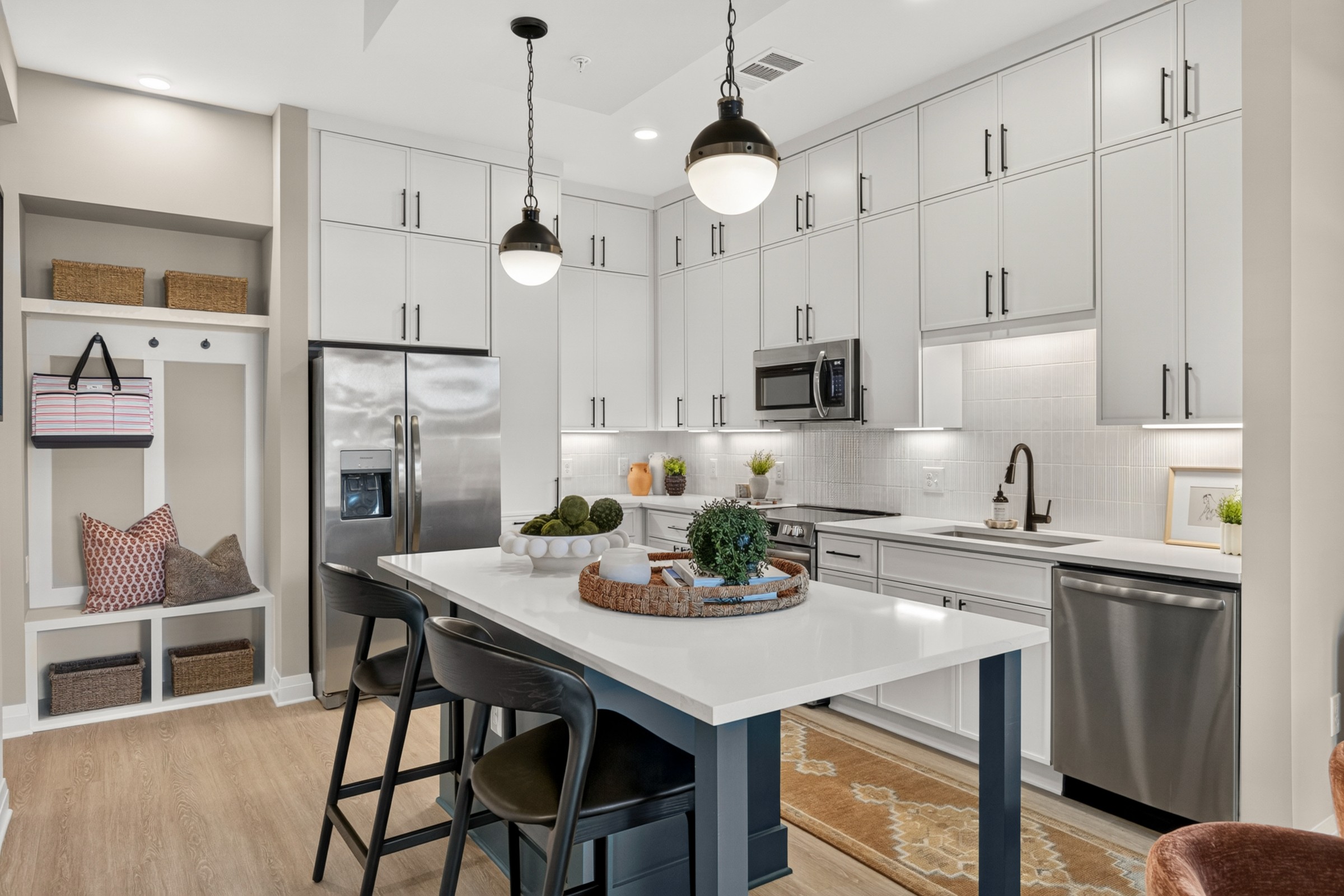 Modern kitchen with white cabinets, stainless steel appliances, and a central island with two black chairs.