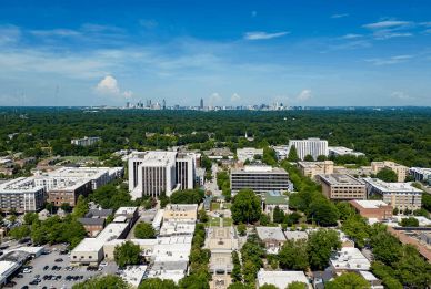 Aerial view of a cityscape with tree-lined streets and tall buildings under a bright blue sky.
